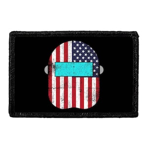 May include: A rectangular patch featuring a central graphic of a welding helmet with a distressed American flag pattern. The helmet has a bright cyan rectangular visor and is set against a solid black background with a thick black border.
