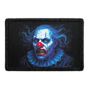 May include: A rectangular embroidered patch featuring a detailed illustration of a clown with blue skin, wild blue hair, and a bright red nose. The clown has a menacing expression with bared teeth and wears a ruffled blue collar against a black background.