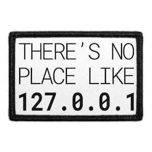 May include: A rectangular patch with a black border and white background. The text "THERE'S NO PLACE LIKE 127.0.0.1" is printed in black, sans-serif font. The patch is likely for clothing or accessories.
