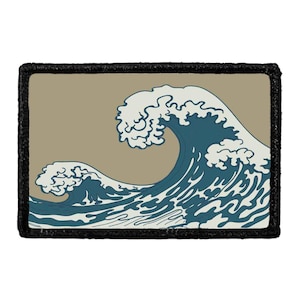 May include: A rectangular patch featuring a graphic illustration of a large, stylized ocean wave in shades of deep blue and off-white against a muted tan background, all enclosed within a thick, textured black border stitched around the edges.