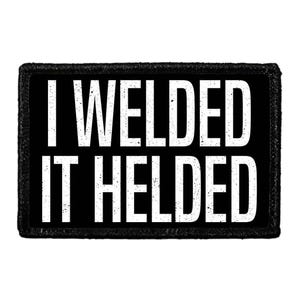 May include: A rectangular black patch with a thick black border. The patch features the white text I WELDED IT HELDED in a bold, sans-serif font. The lettering has a slightly distressed, textured appearance against the solid black background.