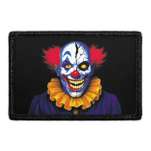 May include: A rectangular embroidered patch featuring a graphic illustration of a clown with a cracked white face, bright red hair, yellow eyes, and a wide grin. The clown wears a yellow ruffled collar and a dark purple garment against a black background.