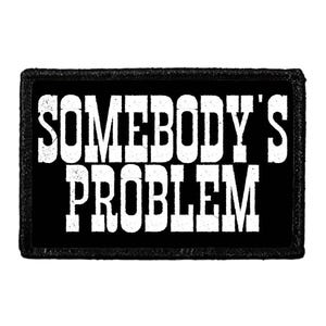 May include: A rectangular black patch with a stitched border featuring the white text SOMEBODY'S PROBLEM in a bold, distressed, serif font. The lettering is arranged in two lines, with the word SOMEBODY'S on top and PROBLEM on the bottom.