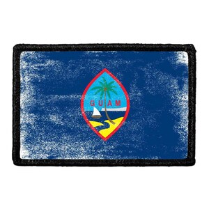 May include: A rectangular patch featuring the flag of Guam with a distressed blue background. In the center, a red-bordered almond-shaped emblem displays a palm tree, a proa boat, and the word GUAM in red letters over a coastal landscape.