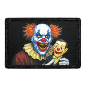 May include: A rectangular patch featuring a menacing clown with orange hair, white face paint, and a red nose. The clown is smiling widely, revealing teeth. Beside the clown is a ventriloquist dummy. The patch has a black border.