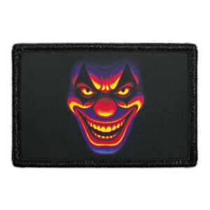 May include: A rectangular black patch featuring a colorful, menacing clown face. The clown's face is a vibrant mix of red, yellow, and purple, with a large, toothy grin and glowing yellow eyes. The patch has a black border.