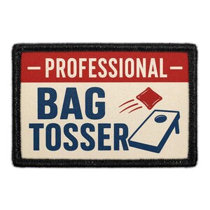 May include: A rectangular patch with a black border featuring a red top stripe with the text - PROFESSIONAL - in white. The cream-colored lower section displays the blue text BAG TOSSER and a blue cornhole board with a red bean bag in motion.
