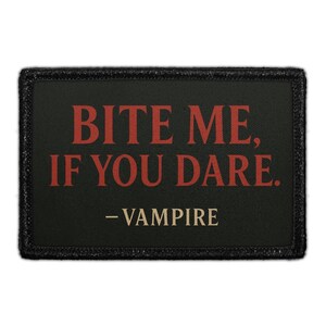 May include: A rectangular black patch with the text "BITE ME, IF YOU DARE." in red letters. Below the text, the word "- VAMPIRE" is written in a smaller, off-white font. The patch has a black border.