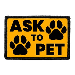 May include: A rectangular patch with a black border and a bright yellow center. The patch features the words "ASK TO PET" in bold black letters, along with two black paw prints.
