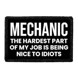 May include: A rectangular black patch with a stitched border featuring the white text MECHANIC THE HARDEST PART OF MY JOB IS BEING NICE TO IDIOTS. The design is centered on a solid black background with bold, sans-serif capital lettering throughout.