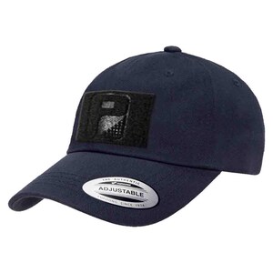 May include: Navy blue adjustable baseball cap with a black square patch featuring a design. The cap has a curved brim and a small button on top. The tag on the front reads "THE AUTHENTIC ADJUSTABLE YUPOONG SINCE 1974".