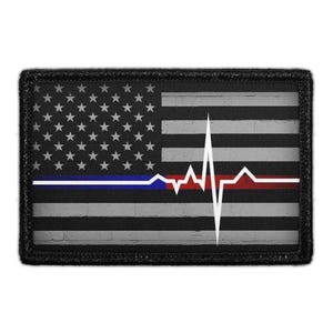 May include: A rectangular patch featuring a grayscale American flag design with a horizontal blue line and a red line integrated into the stripes. A white EKG heartbeat line runs across the center of the flag, superimposed over the stripes.