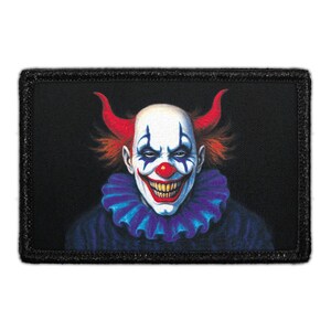 May include: A rectangular embroidered patch featuring a graphic illustration of a clown with a white face, red nose, sharp yellow teeth, and a wide grin. The clown has red hair styled into two horns and wears a dark blue ruffled collar.