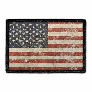 May include: A rectangular patch featuring the United States flag with a distressed, weathered appearance. The design includes a dark blue canton with white stars and alternating red and white horizontal stripes, all bordered by a thick black edge.