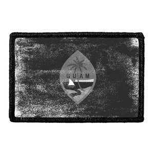 May include: A rectangular patch featuring a distressed, monochromatic black and gray version of the Guam flag. The design includes a central almond-shaped emblem with a palm tree, a proa boat, and the text GUAM, all bordered by a thick black edge.