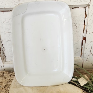 May include: A rectangular white ceramic serving platter with rounded corners and a smooth, glossy finish. The surface shows visible fine crackle patterns throughout the glaze, indicating age and wear on this functional kitchen serving piece.