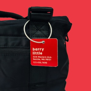 May include: A red luggage tag with the text "barry little" and the address "2315 Western Ave. Seattle, WA 98121" and phone number "123.456.7890".