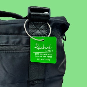 May include: Green luggage tag with white text that reads "Rachel LITTLE", "2315 Western Ave. Seattle, WA 98121", and "123.456.7890".