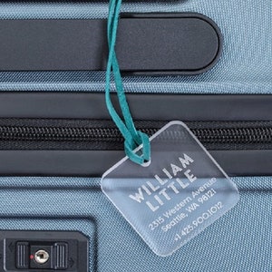 May include: A blue suitcase with a luggage tag that reads "WILLIAM LITTLE 2315 Western Avenue Seattle, WA 98121 +1 425.900.1012"