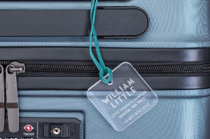 May include: A blue suitcase with a luggage tag that reads "WILLIAM LITTLE 2315 Western Avenue Seattle, WA 98121 +1 425.900.1012"