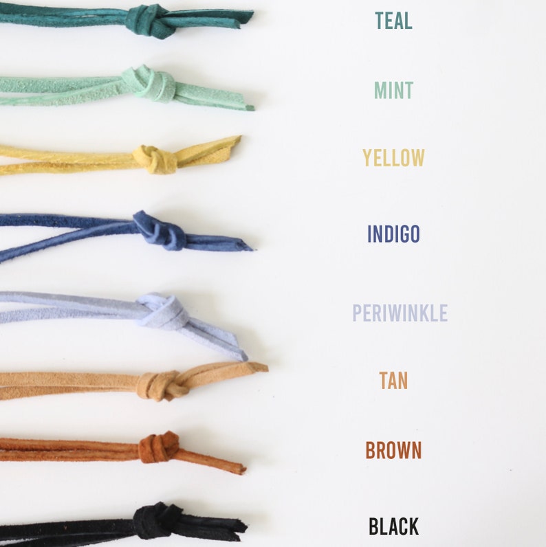 May include: A collection of eight leather cords in various colors, including teal, mint, yellow, indigo, periwinkle, tan, brown, and black. Each cord is tied in a knot and arranged vertically on a white background.