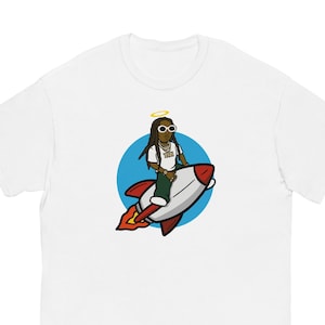 Puede incluir: Camiseta blanca con una ilustración de dibujos animados de una persona con rastas que lleva gafas de sol y un halo, montando un cohete rojo y blanco sobre un fondo de círculo azul.