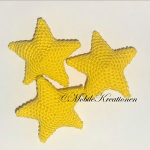 Könnte beinhalten: Drei gelbe gehäkelte Sterne auf weißem Hintergrund. Die Sterne sind aus weichem, strukturiertem Garn gefertigt.