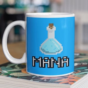 May include: White ceramic mug with a blue background featuring a pixelated image of a blue potion bottle with a cork stopper and the word "MANA" in black pixelated letters.