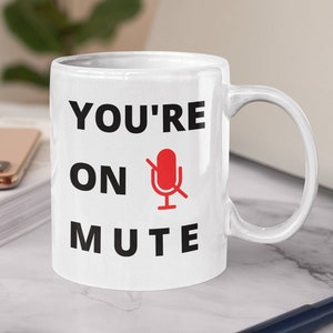 May include: White ceramic mug with black text that reads "You're on mute" and a red microphone icon with a diagonal line through it.