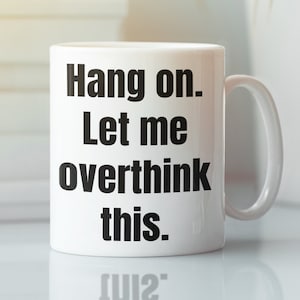 K&ouml;nnte beinhalten: Eine wei&szlig;e Keramik-Kaffeetasse mit schwarzem Text, der "Hang on. Let me overthink this." lautet.