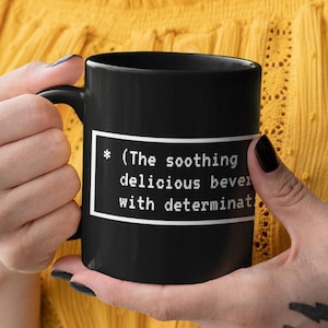 May include: Black coffee mug with a white text box that reads "*(The soothing delicious beverage with determination*"