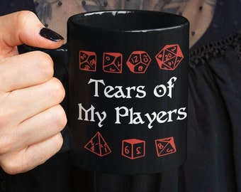 May include: Black coffee mug with white text that reads "Tears of My Players" and red dice graphics around the text.