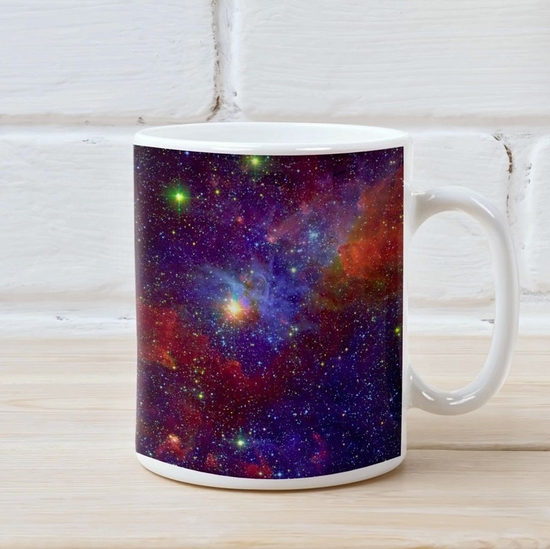 May include: White ceramic mug with a colorful nebula design. The mug features a dark blue background with red, orange, and yellow nebulae and stars.