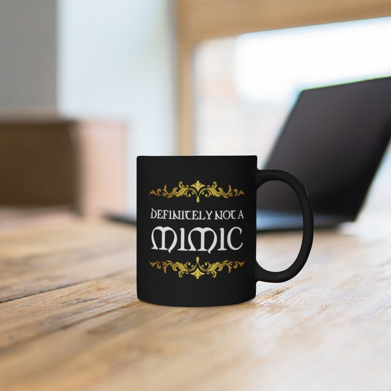 May include: Black coffee mug with gold accents and the text "Definitely not a Mimic" in white.