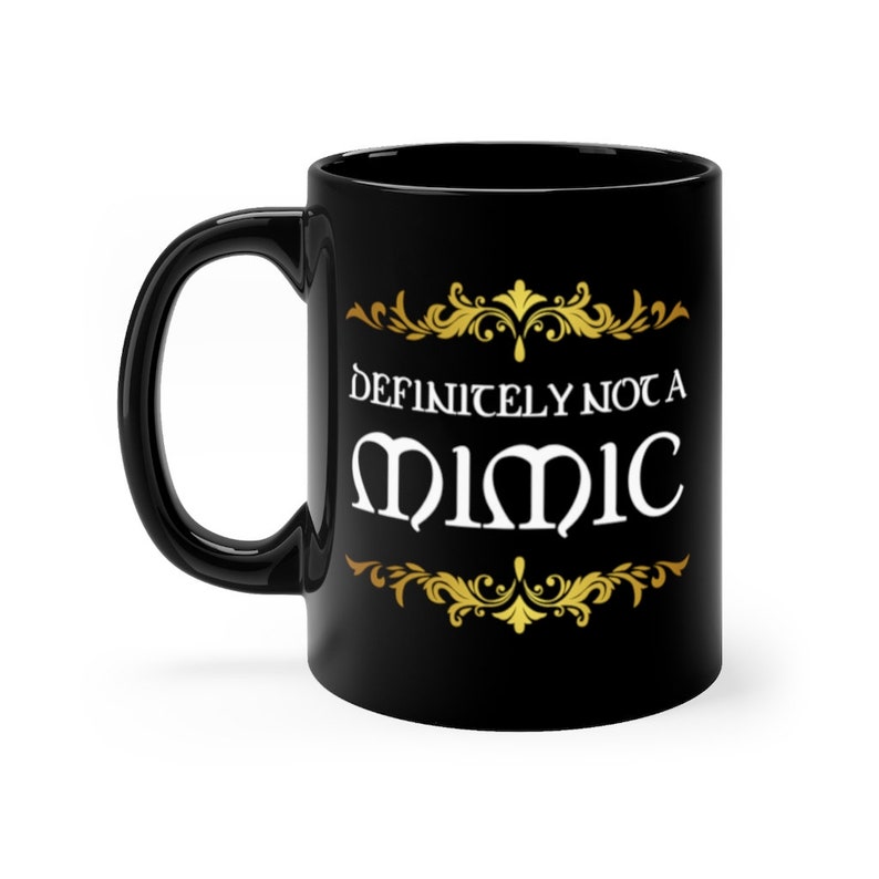 May include: Black ceramic coffee mug with a gold design and the text "Definitely not a Mimic" in white.