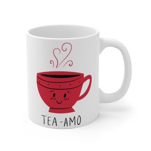 May include: White ceramic mug with a red cartoon teacup with a smiling face and steam coming out of it. The text "TEA-AMO" is printed below the teacup.