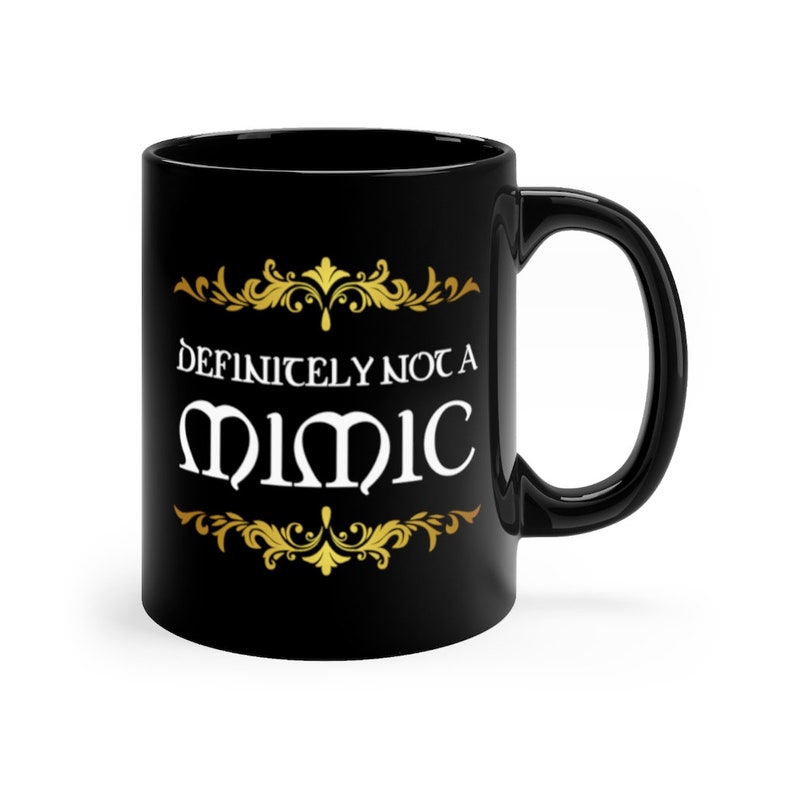 May include: Black ceramic coffee mug with a gold design and the text "Definitely not a Mimic" in white.