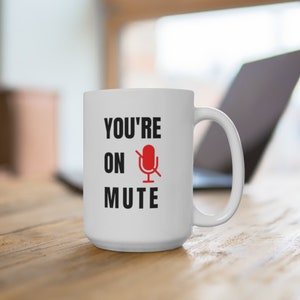 Puede incluir: Taza de caf&eacute; de cer&aacute;mica blanca con texto negro que dice "YOU'RE ON MUTE" y un icono de micr&oacute;fono rojo con una l&iacute;nea diagonal.