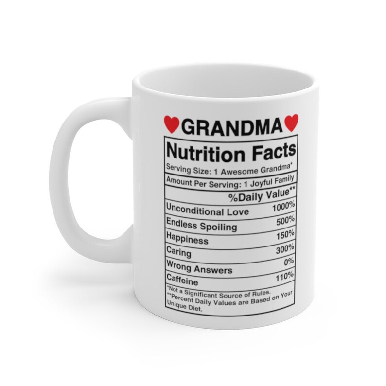 Op de afbeelding: Een witte keramische mok met een rood hart en de tekst "GRANDMA" in zwart. De mok heeft een voedingsschema met humoristische categorie&euml;n zoals "Onvoorwaardelijke liefde" en "Eindeloos verwennen".