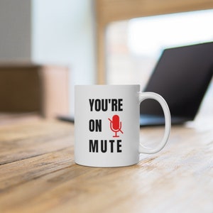 Puede incluir: Taza de cer&aacute;mica blanca con texto negro que dice "You're on mute" y un icono de micr&oacute;fono rojo con una l&iacute;nea diagonal.