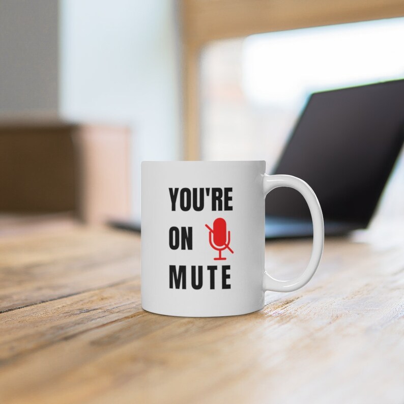 Puede incluir: Taza de cer&aacute;mica blanca con texto negro que dice "You're on mute" y un icono de micr&oacute;fono rojo con una l&iacute;nea diagonal.