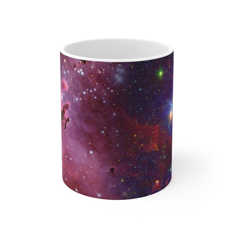 May include: A white ceramic mug with a colorful nebula image printed on it. The nebula is a mix of pink, purple, blue, and yellow colors with a scattering of stars.