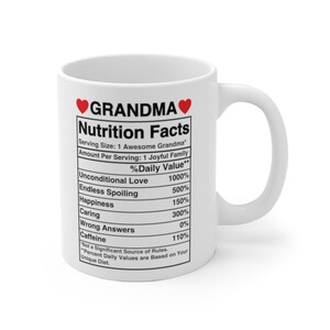 Op de afbeelding: Witte keramische mok met een rood hart en de tekst "GRANDMA" gedrukt op de voorkant. De mok heeft een voedingsschema met humoristische categorie&euml;n zoals "Onvoorwaardelijke liefde" en "Eindeloos verwennen".