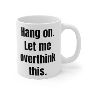 K&ouml;nnte beinhalten: Eine wei&szlig;e Keramik-Kaffeetasse mit schwarzem Text, der "Hang on. Let me overthink this." lautet.