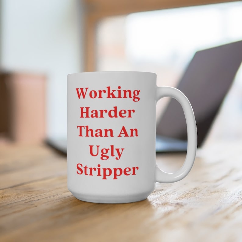 May include: White ceramic coffee mug with the text "Working Harder Than An Ugly Stripper" in red lettering.