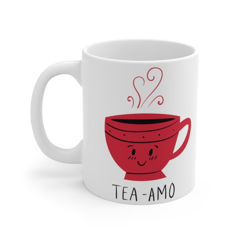 May include: White ceramic mug with a red cartoon teacup with a smiling face and steam coming out of it. The text "TEA-AMO" is printed below the teacup.