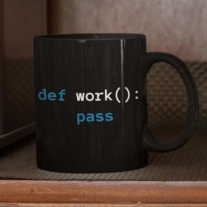 Pu&ograve; includere: Tazza da caff&egrave; nera con il testo "def work(): pass" in lettere bianche e blu. La tazza &egrave; appoggiata su una superficie di legno.