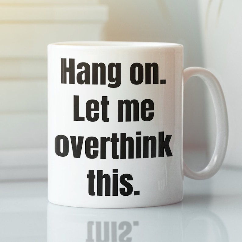 K&ouml;nnte beinhalten: Eine wei&szlig;e Keramik-Kaffeetasse mit schwarzem Text, der "Hang on. Let me overthink this." lautet.
