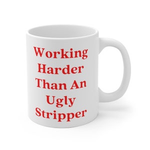 May include: White ceramic coffee mug with the text "Working Harder Than An Ugly Stripper" in red.
