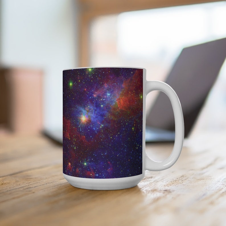 May include: White ceramic mug with a colorful galaxy print. The mug features a nebula with shades of red, blue, and purple, and a scattering of stars.